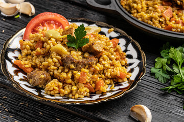 Eastern Uzbek cuisine. Pilaf from Bulgur groats with veal and lamb with carrots. Bulgur pilaf lies in an Uzbek plate with a national pattern on a woody black background.