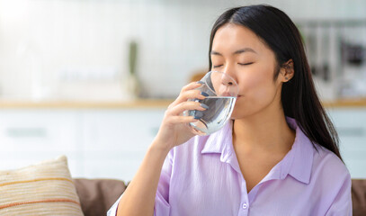 Portrait of young female freelancer drinking clean water sitting at workplace at home on the couch