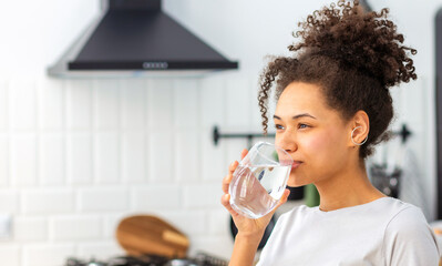 Healthy lifestyle concept. Beautiful young Afro American woman drinking clean water standing at...