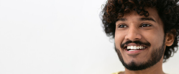 Portrait young happy positive Indian man with white teeth and curly hair smiling broadly on white background, copy space