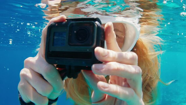 Woman with mask swims underwater with action camera and films a content