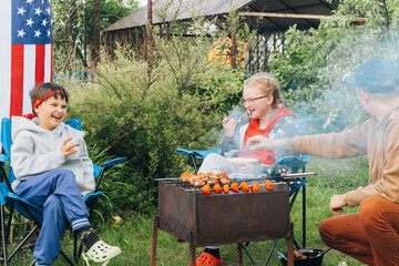 Happy young family make barbecue together in garden. People barbecuing meat on grill. Dad, son,...