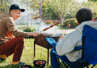 Happy young family make barbecue together in garden. People barbecuing meat on grill. Dad, son,...
