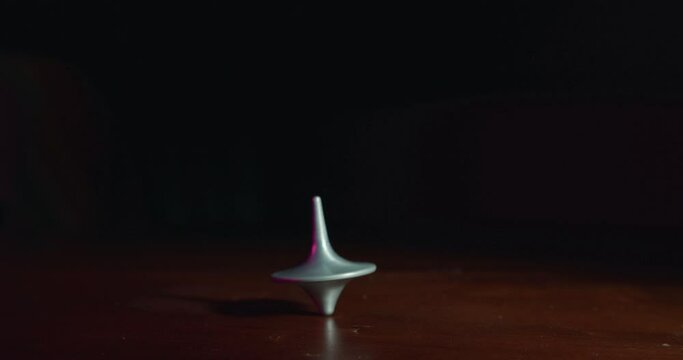 Hand playing with a top spinning on a wooden table in slow motion