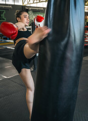 Young asian woman in sportswear and boxing gloves kicking bag in the gym.