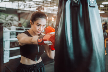 Young Asian woman wearing boxing gloves and hitting the punching bag, Young woman doing boxing...