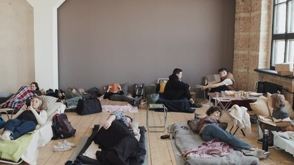 High angle view of women, men and children lying and sitting on sleeping places, talking, using gadgets, reading books and sleeping in afternoon