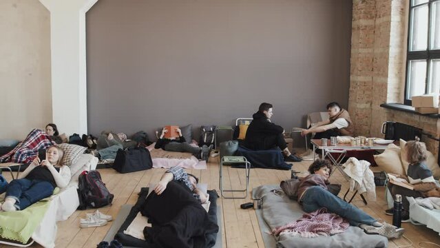 High angle view of women, men and children lying and sitting on sleeping places, talking, using gadgets, reading books and sleeping in afternoon