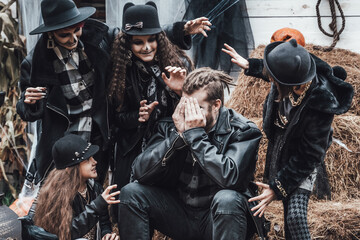 Scary family, mother, father, daughters celebrating halloween. Terrifying black skull half-face makeup and witch costumes, stylish images.Horror,fun at children's party in barn on street.Hats,jackets