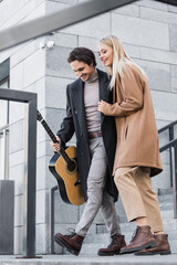 Fototapeta na wymiar joyful and stylish woman walking on stairs near young man with acoustic guitar.