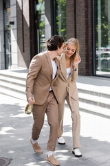 Obraz premium full length of young man with champagne bottle walking near blonde woman on street.