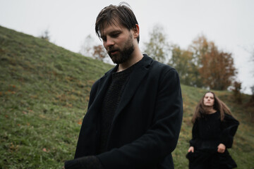 A young couple in love in black coats walks in the countryside in the rain. Autumn gloomy mood. cinematic image