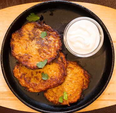 Fried grated potato pancakes with sour cream on frying pan. top of view