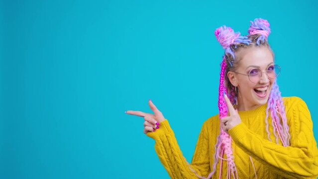 Young colorful girl pointing to the left part of screen (for logo or title) with positive funny emotions, smiling and laughing. Playful feeling, emotional showing to the side. Free space on background