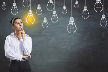 Creativity and idea concept with young pensive woman in white shirt looking at hand drawn white lightbulbs and yellow one switched on