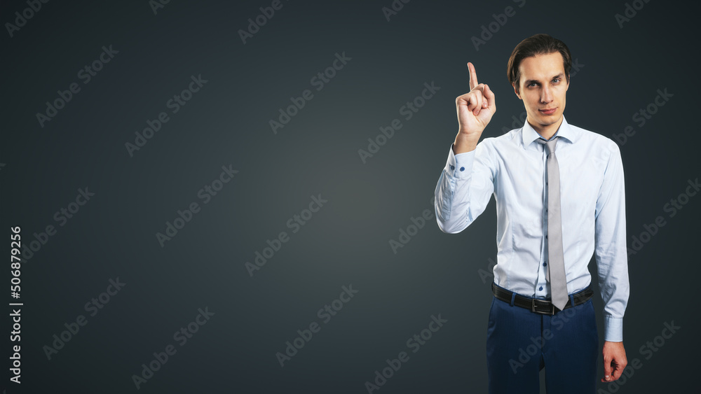 Poster young handsome man in shirt with raising up hand and forefinger isolated on abstract dark grey backg