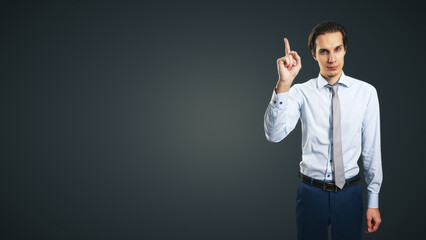 Young handsome man in shirt with raising up hand and forefinger isolated on abstract dark grey...