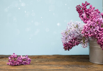 A bouquet of lilacs in an iron bucket on a dark wooden background, highlights, blurry lights and copy space. A branch of purple lilac on a wooden table.