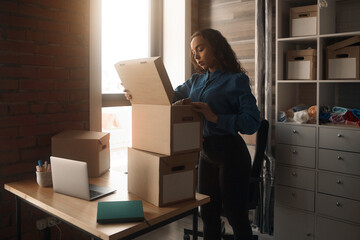 Fototapeta premium Young Asian curly-haired logistics worker packs goods, collects parcels, puts things in a carton box, prepares a parcel for shipment, transports, collects donations, business owner, delivery
