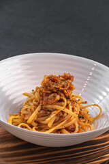 Homemade bolognese noodles with bacon and fried tomato along with ingredients used in the recipe such as tomato and oregano, with a rustic presentation of wooden plates and kitchen utensils