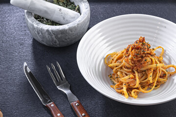 Homemade bolognese noodles with bacon and fried tomato along with ingredients used in the recipe such as tomato and oregano, with a rustic presentation of wooden plates and kitchen utensils