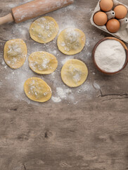 Uncooked stuffed raviolonis or raviolis with flour and ingredients over wooden table with copy space