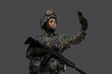 Shot of militant woman dressed in protective suit making selfie against grey background.