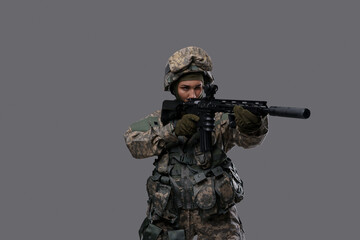Portrait of militant woman dressed in camouflage clothes aiming rifle against gray background.