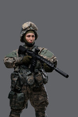 Studio shot of military woman dressed in camouflage clothes and helmet holding rifle.