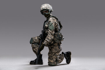 Portrait of soldier woman with rifle sitting on her knee isolated on grey background.