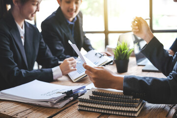 Three Asian business professionals working together and discussing work sitting at conference table in office.