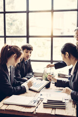 A 50-year-old businesswoman leads a group meeting with colleagues in the boardroom. A variety of colleagues work together to plan a morning briefing. Prepare reports for client teamwork concept.