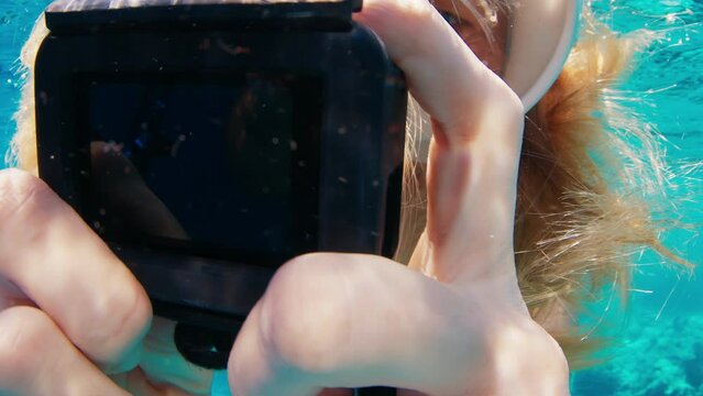 Young woman swims underwater with action camera and films a content