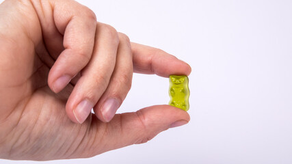 Green rubber candy bear in hand of woman on a white background