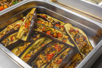 Melanzane grigliate e tagliate a barchetta e ripiene di pomodori in esposizione in una vetrina di una rosticceria