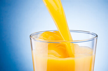 Orange juice pouring into glass on blue background