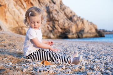 Sweet caucasian baby girl with blond curly hair play on sandy beach with stones by sea.Happy,pretty,adorable,cute toddler,kid spending time on vacation,holiday outdoor at seaside. Kaputas,Kas,Turkey