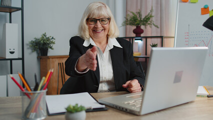 Friendly senior business woman employee outstretching hand to camera offering handshake, greeting with kind smile, welcoming showing solidarity, trust concept. Elderly grandmother freelancer at office © Andrii Iemelianenko