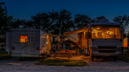 Fototapeta na wymiar Rv motorhomes parked door to door at sunset at the campsite with lights on in the motorhomes 
