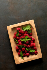 Raspberries and mint leaves, just picked, on wooden tray.