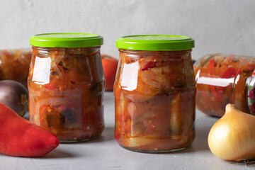 Vegetable salad long-term with eggplant, tomatoes, peppers and onion in glass jars on light gray background