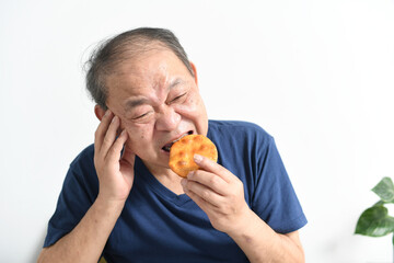 辛い表情で煎餅を食べる高齢者の男性 - obrazy, fototapety, plakaty