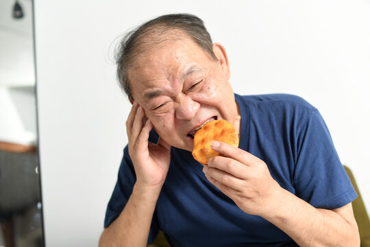 辛い表情で煎餅を食べる高齢者の男性