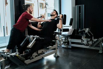 Fototapeta na wymiar A dark-haired guy training leg with his personal trainer