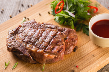 Pork meat steak under barbecue sauce with greens on wooden cutting board
