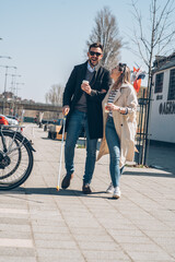 A blind male person using a white cane and walking with his girlfriend.They walk down the...