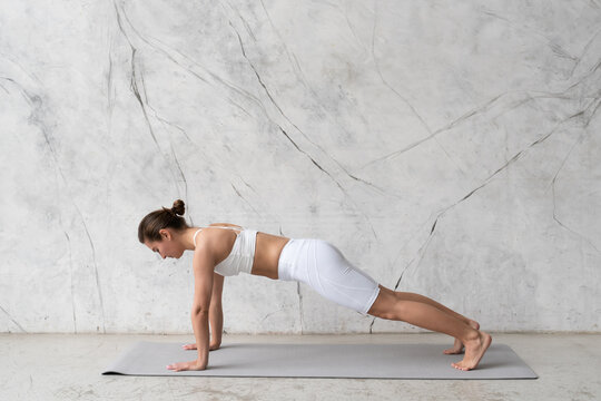 Young woman in white outfit doing plank or practicing dandasana yoga pose