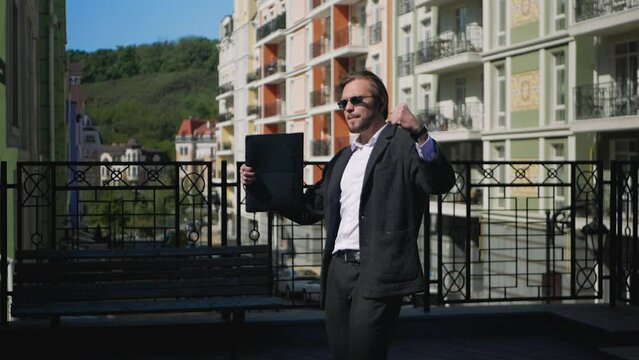 Happy handsome businessman celebrating success and doing a victory disco dance in slow motion. Attractive stylish caucasian man in sunglasses dancing triumphantly after successful business deal.
