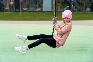 Happy kid girl rids on zip line swing outdoor game play equipment on playground at spring. Child having fun outdoors