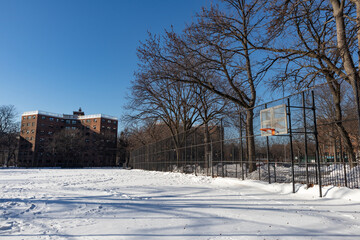 Empty Snow Covered Park with a Basketball Hoop next to Public Housing in Astoria Queens New York during the Winter © James
